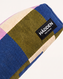 A close-up of a woven pet bed or cushion with a patchwork plaid pattern in blue, olive green, cream, and light pink, featuring a black brand label that reads 'HÄDDEN Pet Home'.