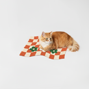 Cat lying on a checkered mat with flower designs on a white background